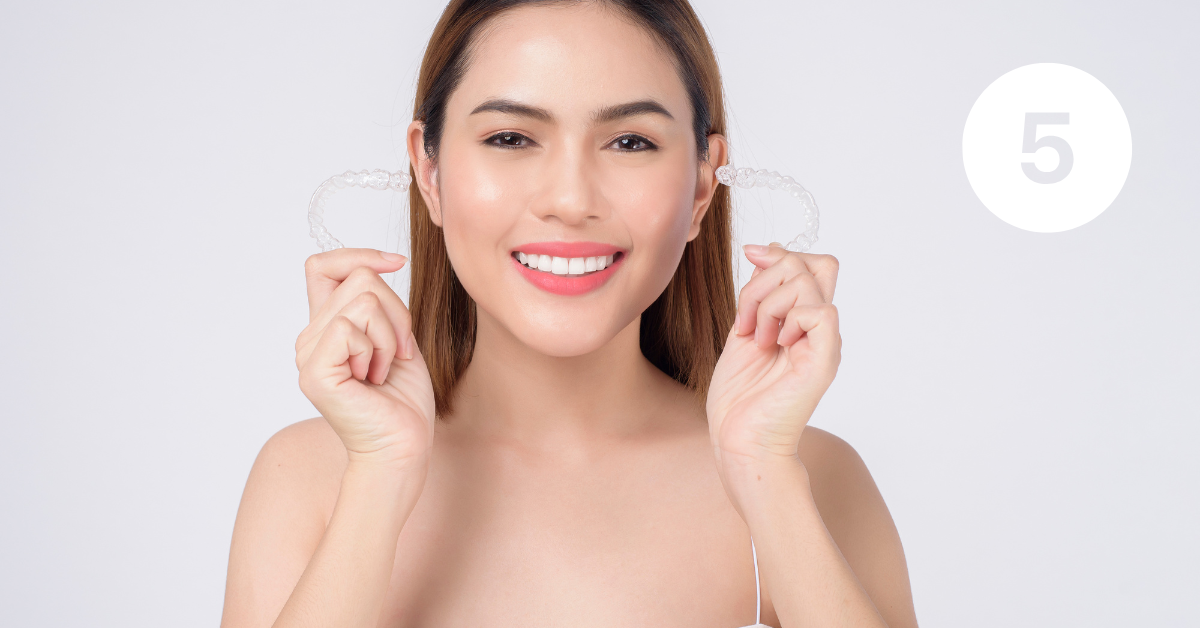 Woman smiling and holding up 2 Invisalign aligners.